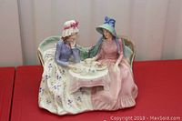 Full front view of the porcelain figurine depicting two women having afternoon tea on a curved bench with detailed tea set on table.