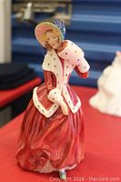 Front view of Royal Doulton Christmas Morn figurine showing detailed red dress, white fur trim, green hat with purple bow