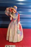 Front view of Royal Doulton Miss Demure porcelain figurine showing detailed clothing and face, standing on a red surface.