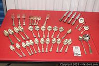 Full layout of the Birks silver plate cutlery and sterling serving pieces arranged on red surface, showing all knives, forks, spoons, and serving pieces clearly.