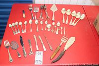 Full assortment of cutlery arranged on red background showing spoons, forks, butter knives, serving utensils, and button hook