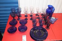 Full view of blue glassware set on red table including plates, bowls, various goblets, and teapot.