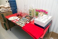 Full view of lot items on red table including glass vases, cranberry glass tumblers, placemats with coasters, boxed wine glasses, and candy dishes