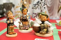 Three Goebel Hummel figurines on display: two standing children and one seated child with rabbits.
