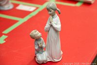Photo of Lladro porcelain figurine showing front view of two praying children, one girl standing, one boy kneeling on red background.