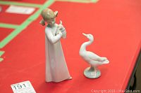 Photo shows both Lladro figurines on a red surface: the girl figurine holding a bird and the goose figurine standing on a base.