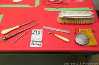 Overview of entire set on red surface showing clothes brush, manicure items, button hook, folding ruler, and sterling silver compact in soft pouch.