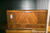 Left side view of the cedar lined wooden chest showing the chevron veneer, rounded edge top, and carved bottom trim.