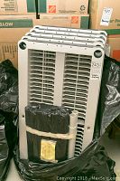 Photo of stacked white plastic shelving units with black plastic garbage bags and white tubes strapped in front.