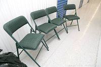Four green Cosco folding chairs arranged in a storage unit showing upholstery and structure