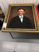 Full frontal view of framed oil portrait of a man in black suit and blue tie
