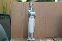 Front view of a Lladro figurine, showing a girl holding a lamb in her arms against a cardboard background.