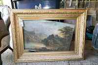 Full view of oil painting leaning against a surface, showing the ornate frame and overall condition.