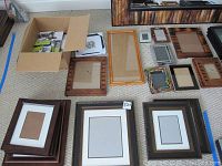 Overview of various frames laid out on floor, including wooden and plastic frames, some matted.