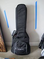 Soft padded black Roland Grassroots branded guitar case standing upright against a wall.