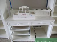 Wide view of white desk showing two drawers, two rolling trays open on the left, and open space on the right with cable hole. Two white compartment organizers placed on the top surface of the desk.