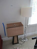 Desk lamp with rectangular burlap shade and black base, positioned next to metal floor lamp with white woven round shade in room corner.