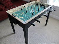 Full view of foosball table with black and white players, green playing field, black legs, and black handles.