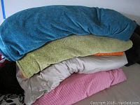 Five duvet covers stacked, showing various colors and textures, top teal, green with orange fur, beige satin backing, pink gingham bottom.
