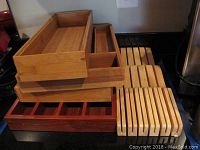 Photo of stacked bamboo flatware organizers, wooden knife rack, and two wooden slotted trivets or pot holders next to a stove and counter.