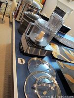 Photo showing Cuisinart food processor and two large stock pots with glass lids on a table.