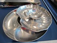 Silver color serving dishes arranged showing clam shell bowl, lazy Susan with etched design, and small handled bowl on a hammered silver platter.