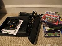 Xbox 360 console, Kinect sensor, controller, and stacked games on carpeted floor.