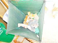 Top view photo of 7 assorted stuffed toys inside a green mesh basket including a gray koala and a light brown bear with plaid accents.