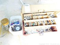 Plastic toolbox with dividers and multiple compartments filled with assorted screws, nuts, bolts, and wood dowels. Also visible are small plastic containers with hardware items.