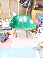 Front view of steel wheelbarrow showing green tray with paint chipping and wooden handles