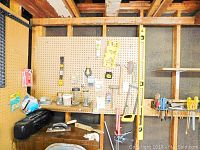 Overview of pegboard and shelves with various hand tools and hardware including jars of nails, saw, hammers, and levels.