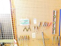 Photo of pegboard displaying multiple screwdrivers, pliers, a clear plastic box containing screws, and yellow-striped spirit level.