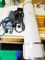 Fluorescent lamp lying horizontally on a wooden surface with three black power bars with cords coiled beside it.