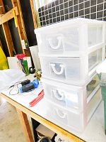 Stack of four clear plastic storage drawers on a wooden table with various camera accessories inside.