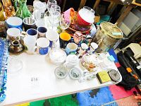 Wide view of assortment of kitchen items on table including mugs, teapots, ice bucket, and Blue Mountain Pottery plate