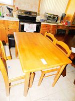 Wide view of wooden dining table with four chairs in a kitchen setting, showing overall condition and style.