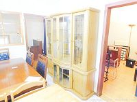 Two-piece wood and glass china cabinet positioned next to dining table and chairs, showing full front view of cabinet with glass doors and wood base doors.