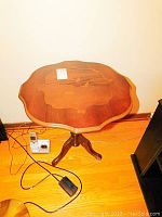 Top view of wooden square accent table showing decorative inlay and curved edges with floor plugs and cords nearby.