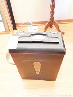Black Aurora AS860C paper shredder on hardwood floor with handle and control buttons visible.