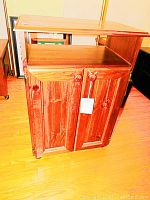 Front view of wood cabinet showing two paneled doors with wooden knobs and reddish-brown finish.