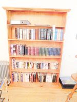 Full front image of wooden bookcase filled with books and a file binder on top shelf; contents will not be included in sale.