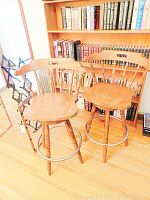 Two wooden bar stools shown side by side in front of a bookshelf, highlighting their seats, backrests, and legs.