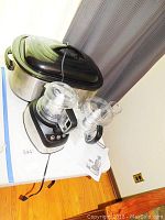 Photo showing Rival stainless steel roaster with black lid on top, alongside Black & Decker food processor with clear plastic bowl and black stainless base.