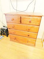 Full front view of the wood dresser showing all four drawers and wooden knobs, some visible staining and scratching on drawer fronts and base.