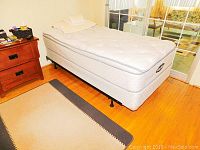 Single bed set with Body Zone mattress and box spring in a room shown from side angle, on wooden floor near nightstand and glass door.