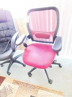 Front view of red mesh back office chair with cushioned seat next to a black padded office chair.