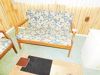 Full front view of wood frame loveseat with blue floral patterned cushions placed on a carpeted floor against a wood-paneled wall.