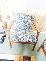 Front view of wood and fabric lounge chair showing floral cushions and wooden armrests.