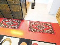 Two carpets laid side by side on the floor, each showing similar red base colors and complex traditional patterns