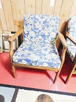 Wood and fabric armchair with blue floral patterned cushions against wood panel wall, showing full chair front view.